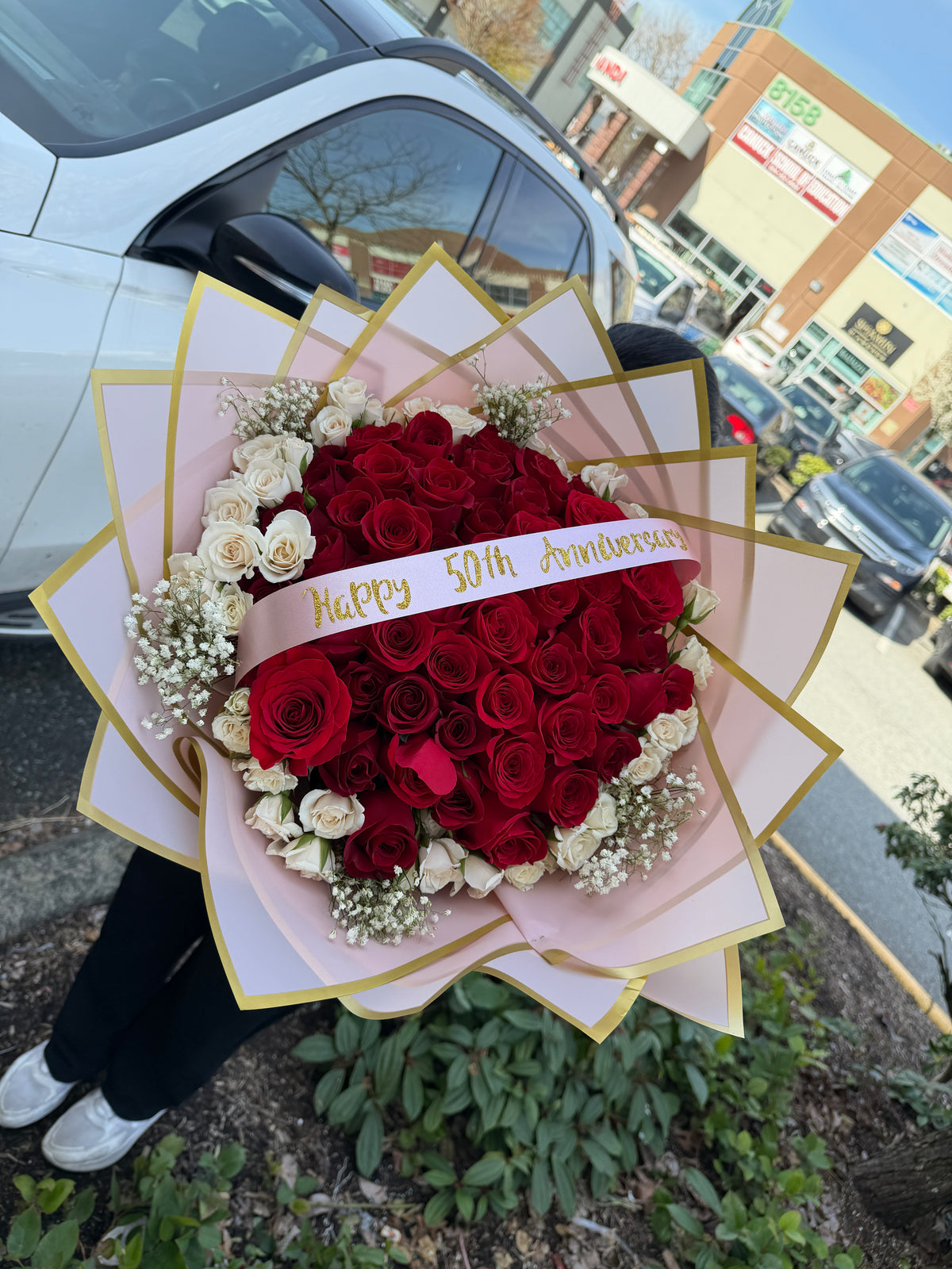Close-up of 50 red roses bouquet with spray white roses and baby’s breath, pink and gold wrapping, luxury floral arrangement – Roses Canada
